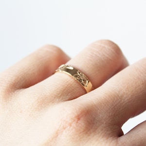 Puede incluir: Un anillo dorado con un dise&ntilde;o floral. El anillo, usado en un dedo, presenta un dise&ntilde;o detallado de flores y hojas. El anillo es de metal y est&aacute; ligeramente curvado. El dise&ntilde;o del anillo es visible.