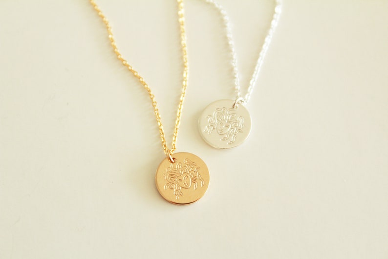 K&ouml;nnte beinhalten: Zwei Halsketten mit runden Anh&auml;ngern, die ein detailliertes, graviertes Bild eines Frauenkopfes zeigen. Eine Halskette hat eine goldene Kette und einen Anh&auml;nger, die andere eine silberne Kette und einen Anh&auml;nger.