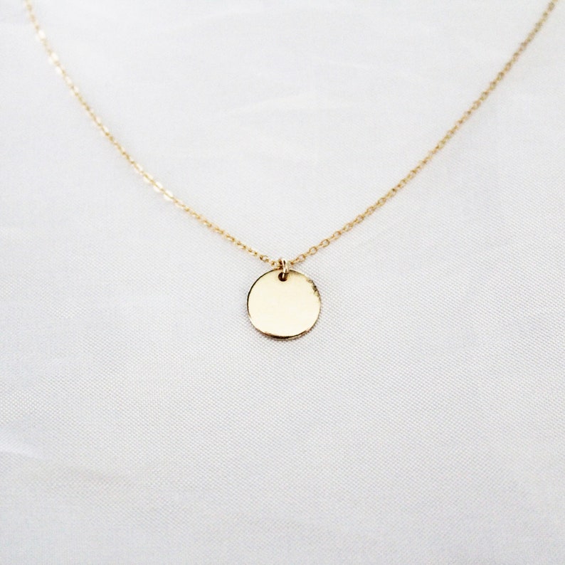 Puede incluir: Un collar de cadena de oro con un peque&ntilde;o colgante redondo.