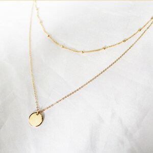 May include: A gold layered necklace with a round pendant. The necklace is on a white background.