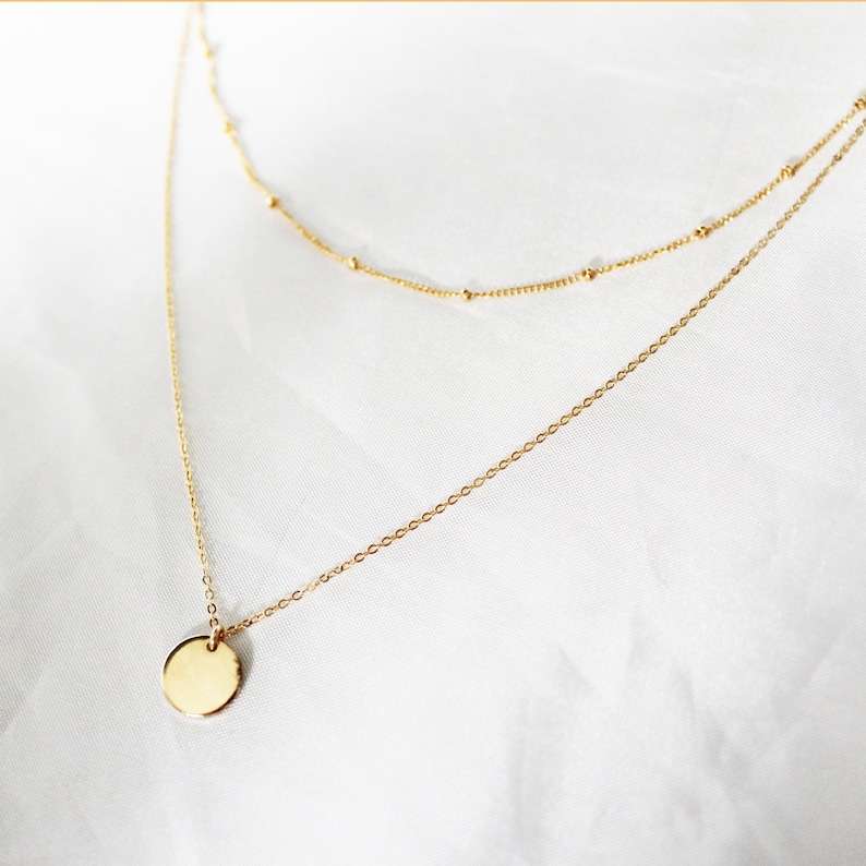 May include: A gold layered necklace with a round pendant. The necklace is on a white background.