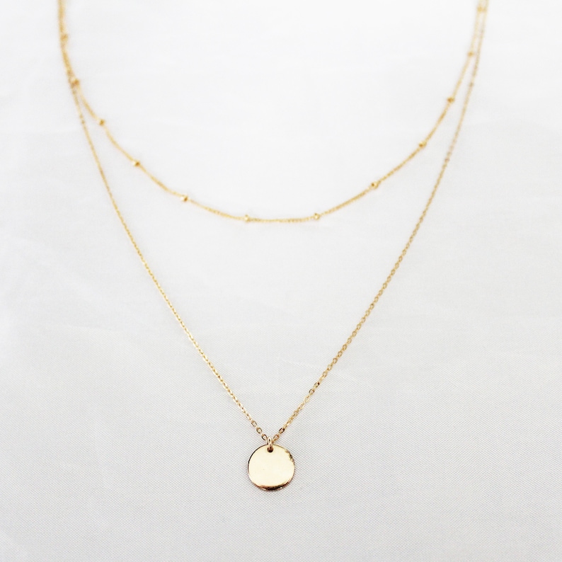 May include: A gold layered necklace with a round pendant. The necklace is made of delicate chains.