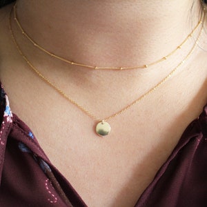 May include: A gold chain necklace with a small, round pendant. The necklace is layered with a thinner chain.