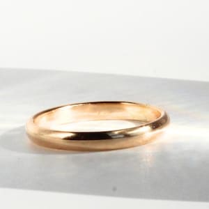 Könnte beinhalten: Ein polierter Ring aus Roségold mit einer glatten, abgerundeten Oberfläche und einer durchgehenden Kreisform. Das Metall hat einen warmen, metallisch-rosa Farbton, der das Licht auf seiner gewölbten Außenseite reflektiert und ein schlichtes Design erzeugt.