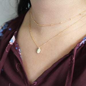 May include: A gold chain necklace with a small, round pendant. The necklace is layered with a second, thinner chain.