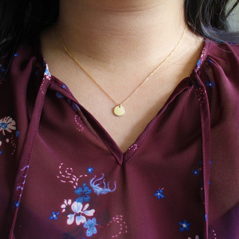 Puede incluir: Un collar sencillo de oro con un peque&ntilde;o colgante redondo. El collar lo lleva una persona con el pelo oscuro y una blusa burdeos con estampado floral.