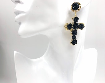 May include: A dangling earring featuring a gold-tone filigree cross adorned with multiple small black rose-shaped beads. The earring includes a matching circular stud component at the top, also decorated with a single black rose and gold filigree.