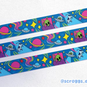 May include: Blue decorative tape with a repeating pattern of green aliens, planets, UFOs, and cows. The aliens are giving the peace sign. The design includes stars and colourful rainbow streaks. The tape is labelled with the text "@scroggs_art".