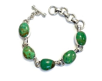 May include: A silver bracelet featuring five oval-shaped green turquoise stones. The bracelet has a toggle clasp.