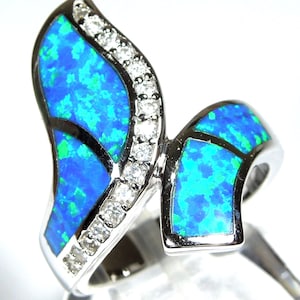 May include: A silver ring featuring a blue and green opal stone set in a wave-like design. The ring is accented with clear cubic zirconia stones.