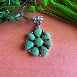 May include: A silver pendant featuring a cluster of turquoise stones. The stones are a vibrant turquoise color with brown matrix patterns. The pendant has a decorative bail and a circular arrangement of stones, perfect for a necklace.