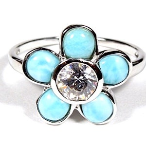 May include: A silver ring with a flower design featuring five blue turquoise stones and a clear center stone.