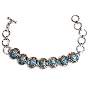 May include: A silver bracelet with a toggle clasp and six oval-shaped charms. The charms are decorated with a blue and orange floral pattern.