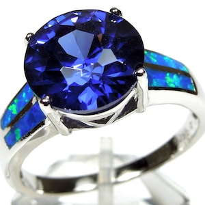 May include: A silver ring with a large blue gemstone and two smaller blue opals on the band.