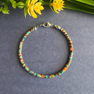 May include: A delicate bracelet composed of small, flat, circular beads in vibrant shades of turquoise, orange, and brown. The bracelet features a silver-toned metal lobster claw clasp and two small silver-toned metal beads near the closure.