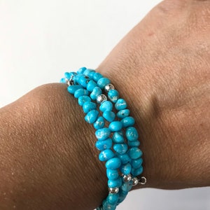 Puede incluir: Un brazalete de cuentas turquesa y plata con múltiples hebras. El brazalete está hecho de pequeñas cuentas turquesa irregulares con detalles plateados.