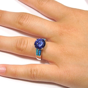 Pu&ograve; includere: Un anello d'argento con una grande pietra preziosa blu circondata da due bande di opale blu.