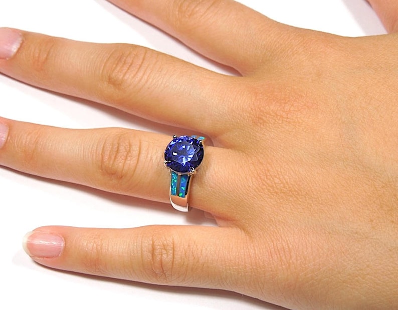 Pu&ograve; includere: Un anello d'argento con una grande pietra preziosa blu circondata da due bande di opale blu.