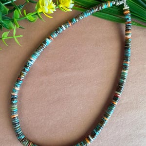 Peut inclure: Un collier composé de petites perles plates et circulaires dans une variété de couleurs, notamment turquoise, marron, orange et blanc. Les perles sont disposées selon un motif répétitif le long du cordon, doté d'un fermoir en métal argenté.