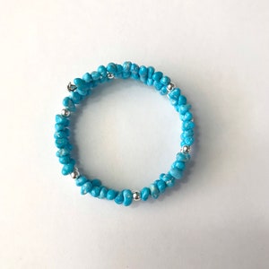 Könnte beinhalten: Ein türkisfarbenes Armband mit silbernen Perlen. Das Armband besteht aus kleinen, unregelmäßigen türkisfarbenen Perlen und silbernen Zwischenperlen.