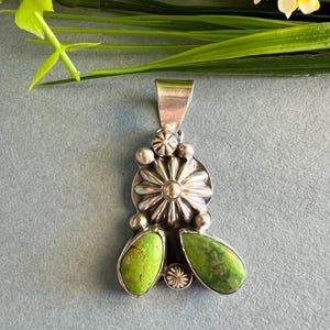 May include: A silver pendant featuring a green turquoise stone and a silver flower design.