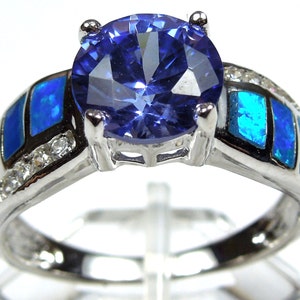 Può includere: Un anello d'argento con una grande pietra preziosa blu circondata da pietre blu più piccole e dettagli bianchi.