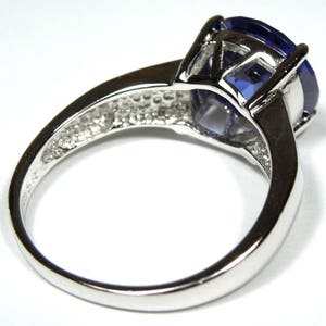 Pu&ograve; includere: Un anello d'argento con una grande pietra preziosa ovale di colore blu scuro. L'anello ha una fascia semplice e una montatura a griffe.