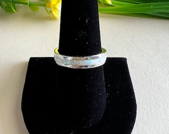 May include: A silver ring with a white opal inlay. The ring is displayed on a black ring holder.