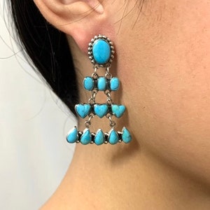 以下が含まれることがあります： シルバーのセッティングにターコイズのドロップイヤリング。イヤリングは、レイヤーデザインの涙のしずくの形をしています。