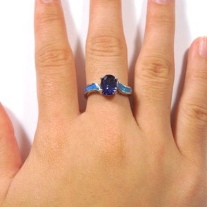 May include: A silver ring featuring a blue oval gemstone and blue opal accents.