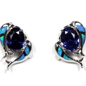 Könnte beinhalten: Ein Paar silberne Ohrringe mit einem blauen Edelstein, umgeben von einem Design aus zwei Delfinen mit blauen und grünen Opal-Akzenten.
