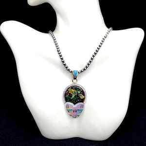 May include: A silver chain necklace with a skull pendant. The skull is made of iridescent abalone shell and has a colorful inlay of turquoise, coral, and other stones. The inlay depicts a bird in flight.