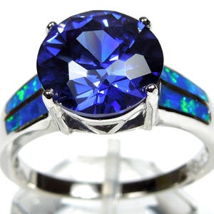 Pu&ograve; includere: Un anello d'argento con una grande pietra preziosa blu circondata da due bande di opale blu e verde.