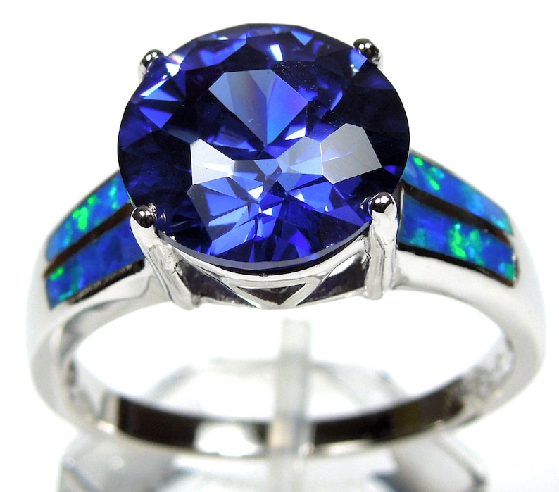 Pu&ograve; includere: Un anello d'argento con una grande pietra preziosa blu circondata da due bande di opale blu e verde.