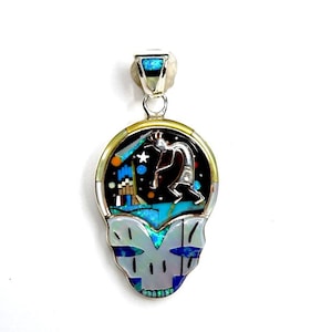 Op de afbeelding: Een zilveren hanger met een rond, veelkleurig inlegontwerp. De inleg toont een indiaanse figuur, sterren en geometrische vormen. De hanger is gemaakt van sterling zilver en is bezet met turquoise, koraal en andere stenen.