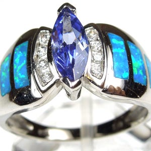 Può includere: Un anello d'argento con una pietra preziosa blu a forma di marquise circondata da pietre preziose più piccole e trasparenti. La fascia è decorata con inserti di opale blu e verde.