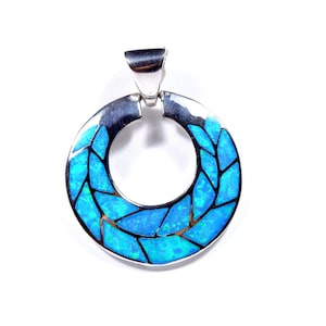 May include: A silver pendant with a circular design featuring a blue opal inlay. The opal is cut into small, irregular shapes that create a mosaic-like pattern.