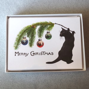 Op de afbeelding: Set kerstkaarten met een zwarte kat die een tak met ballen vasthoudt. De tak heeft groene naalden en kleurrijke ballen. De woorden "MERRY CHRISTMAS" staan eronder gedrukt.