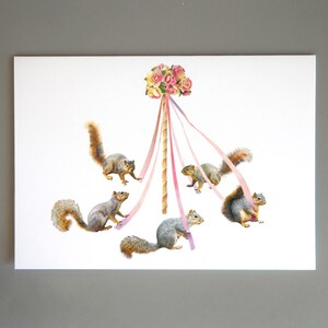 May include: Five gray squirrels are playing around a maypole decorated with pink and white ribbons and a bouquet of pink and yellow flowers.