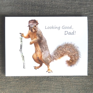 May include: A greeting card featuring a squirrel wearing a brown hat and holding a stick. The text on the card reads "Looking Good, Dad!"