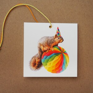 May include: A brown squirrel wearing a colorful party hat sits on top of a large, rainbow-colored paper ball.