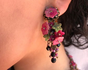 May include: Pink and green flower-shaped earrings with black beads dangling from the bottom.