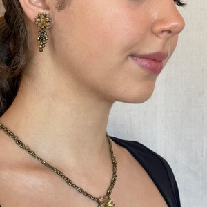May include: A gold-toned jewellery set featuring a floral design. The set includes a necklace with a pendant and matching earrings. The earrings and pendant have a cluster of small beads. The necklace chain is made of small, connected beads.