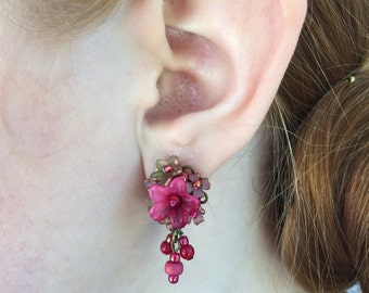 May include: Pink flower earrings with dangling beads. The earrings are made of glass and metal.