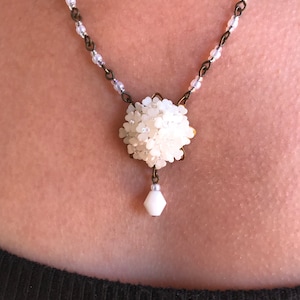 May include: A white beaded necklace with a large white flower pendant and a single white teardrop bead.