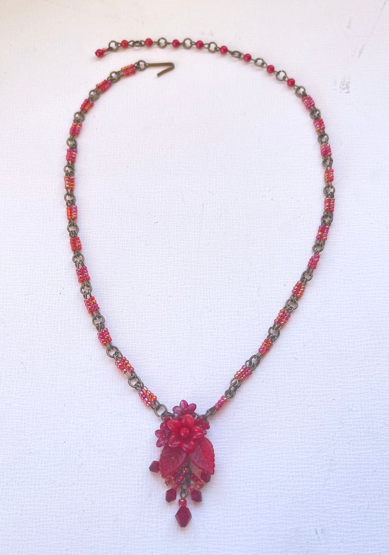 May include: A red beaded necklace with a red flower pendant and crystal accents.