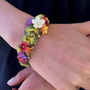 May include: A colorful floral bracelet with a variety of flowers, including white, yellow, red, orange, purple, and green. The bracelet is made of metal and has a delicate chain.