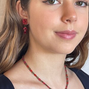 May include: A red beaded necklace with a floral pendant and matching earrings. The necklace and earrings are made of small red beads and have a vintage look.