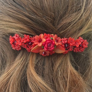 May include: Red floral hair comb with a large red rose and smaller red flowers. The comb is made of beads and has a gold metal clip.