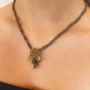May include: Vintage brass-coloured necklace with a floral pendant, leaves, and grape-like clusters. The chain is made of small, connected links. The necklace is worn around the neck.